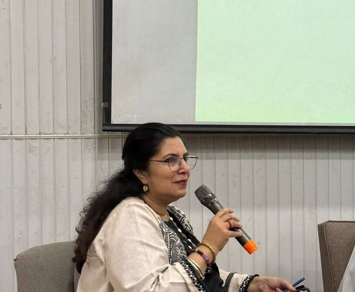 Naela Aamir standing beside one of her framed blossom paintings at an exhibition